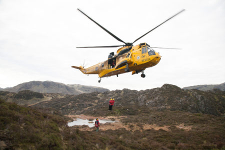 An RAF Seaking winching Mountain Rescue Team members from a mountain side